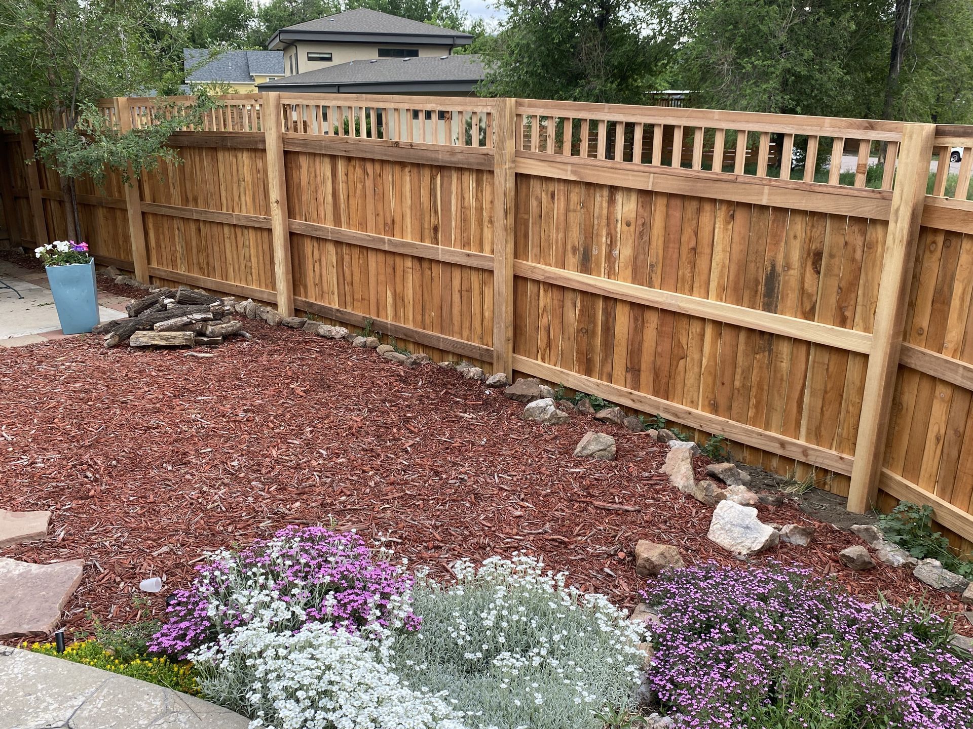 A wooden fence is surrounded by rocks and flowers in a backyard.