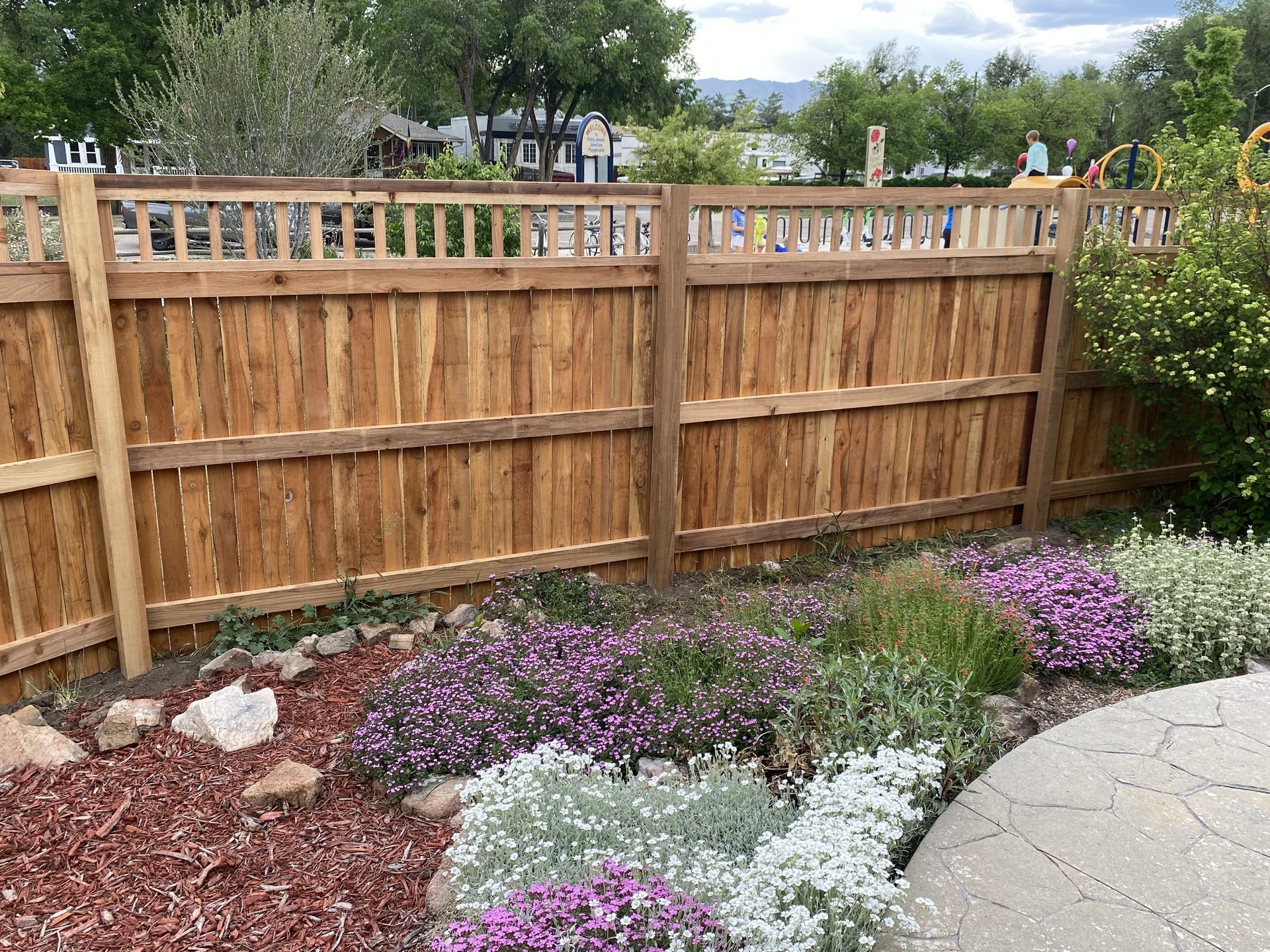 A wooden fence is surrounded by flowers and rocks in a garden.