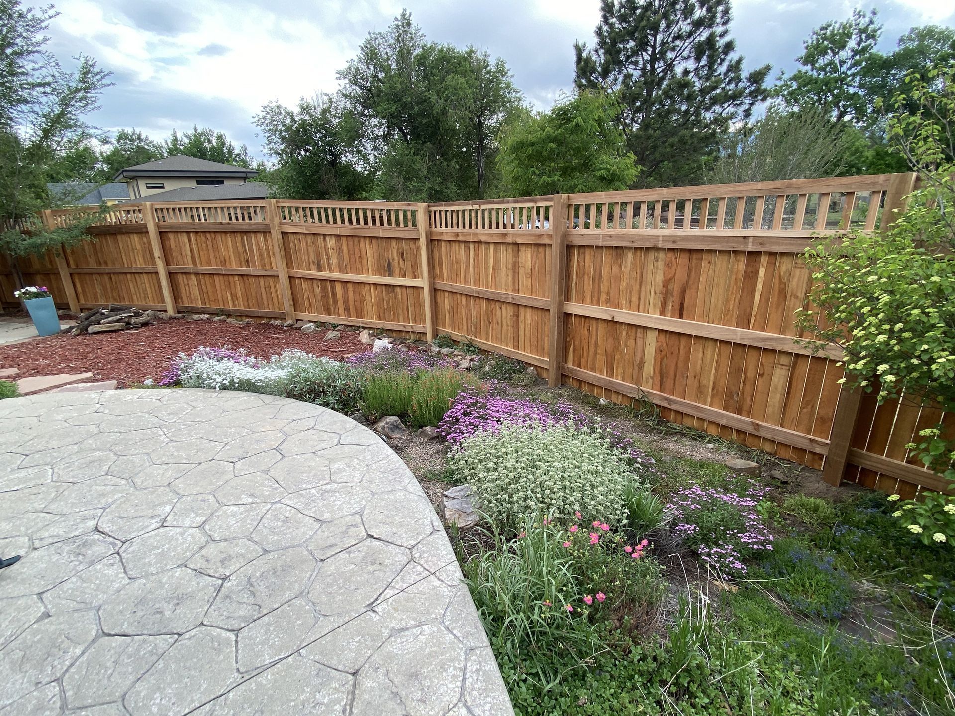 A wooden fence is surrounded by flowers and trees in a backyard.