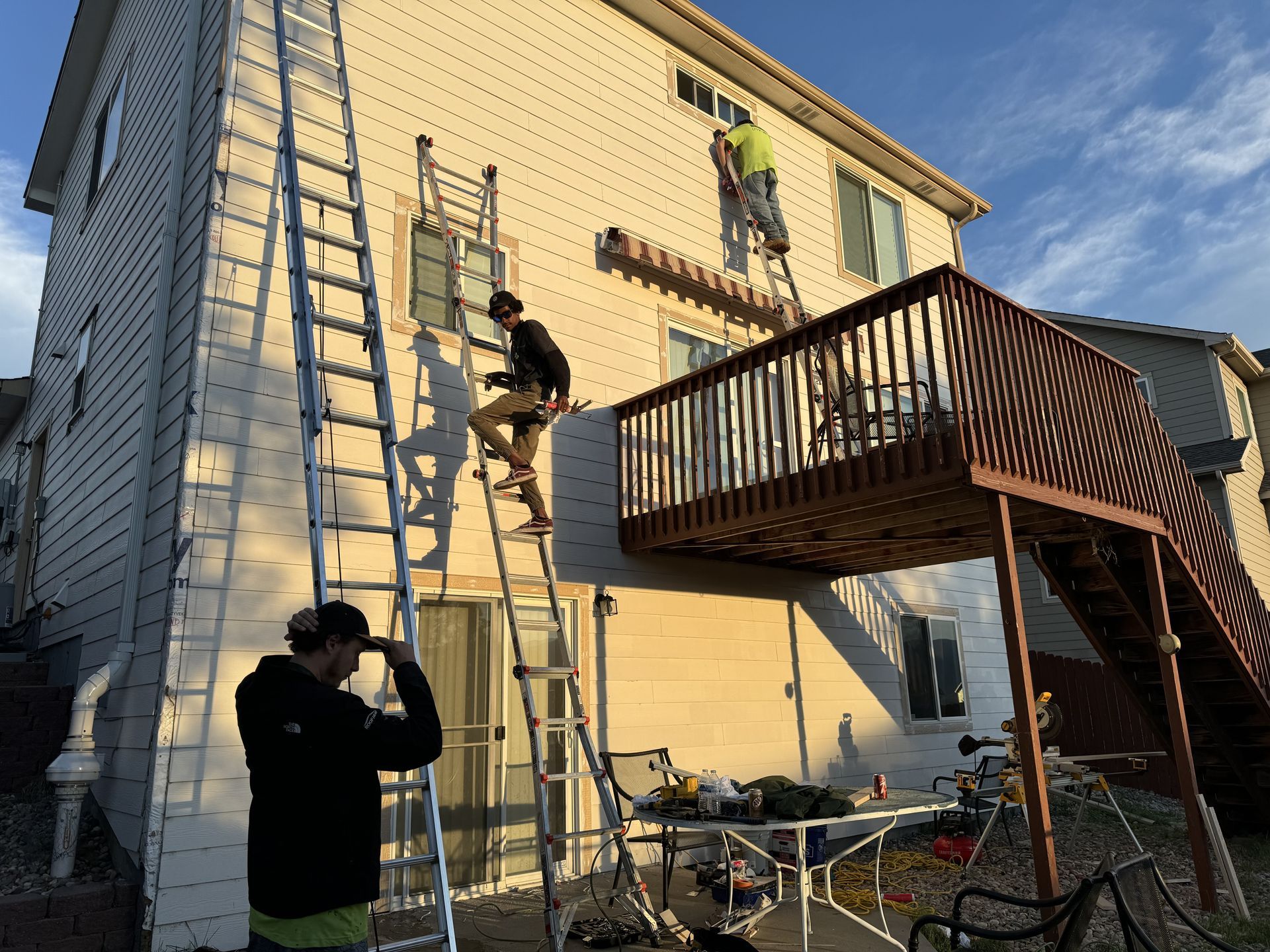 Two men are painting the side of a house with ladders.