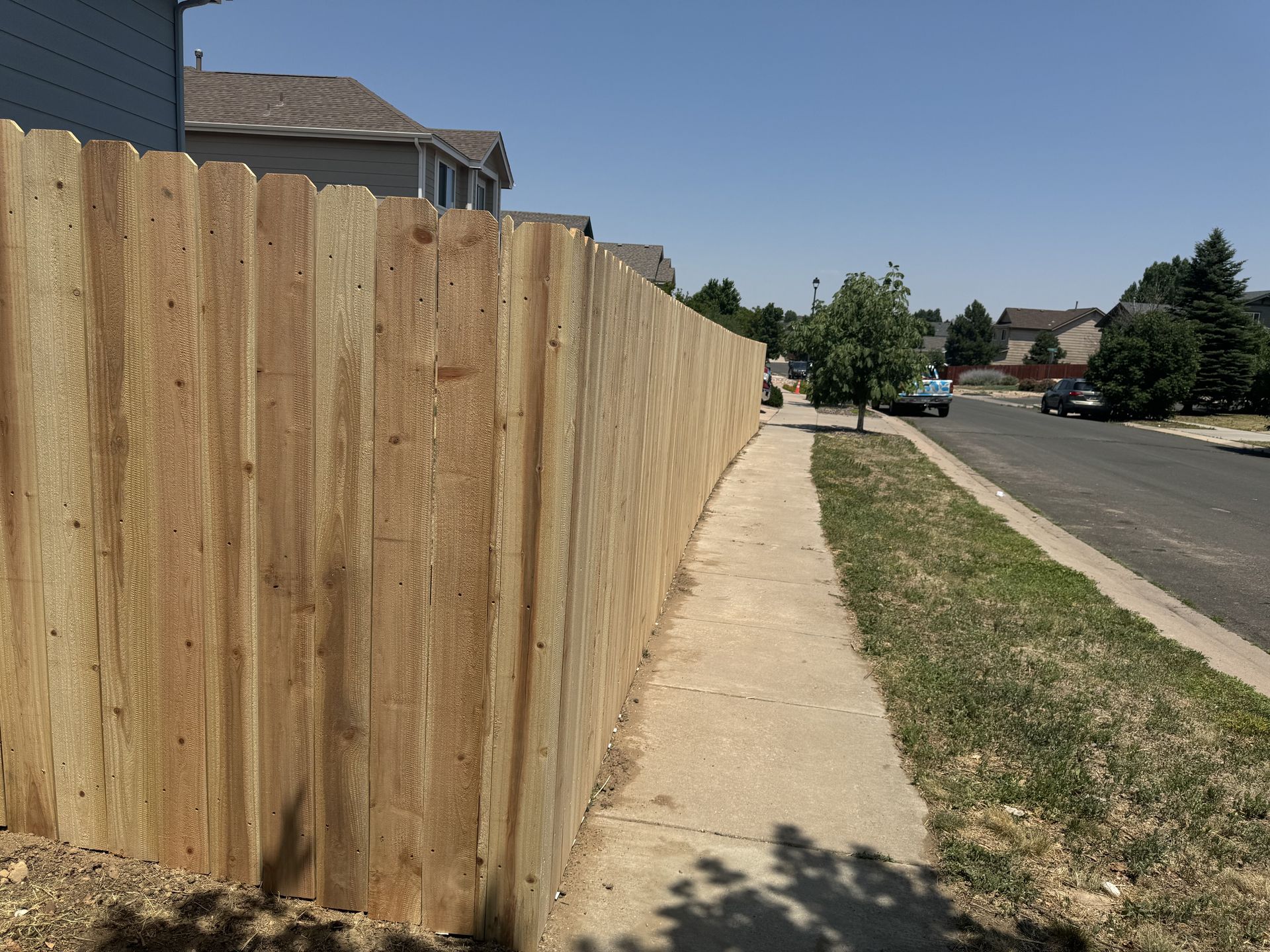 A wooden fence along a sidewalk in a residential neighborhood.