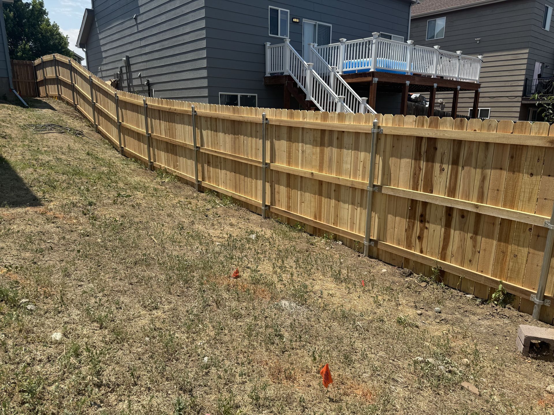 A wooden fence is sitting on top of a grassy hill in front of a house.