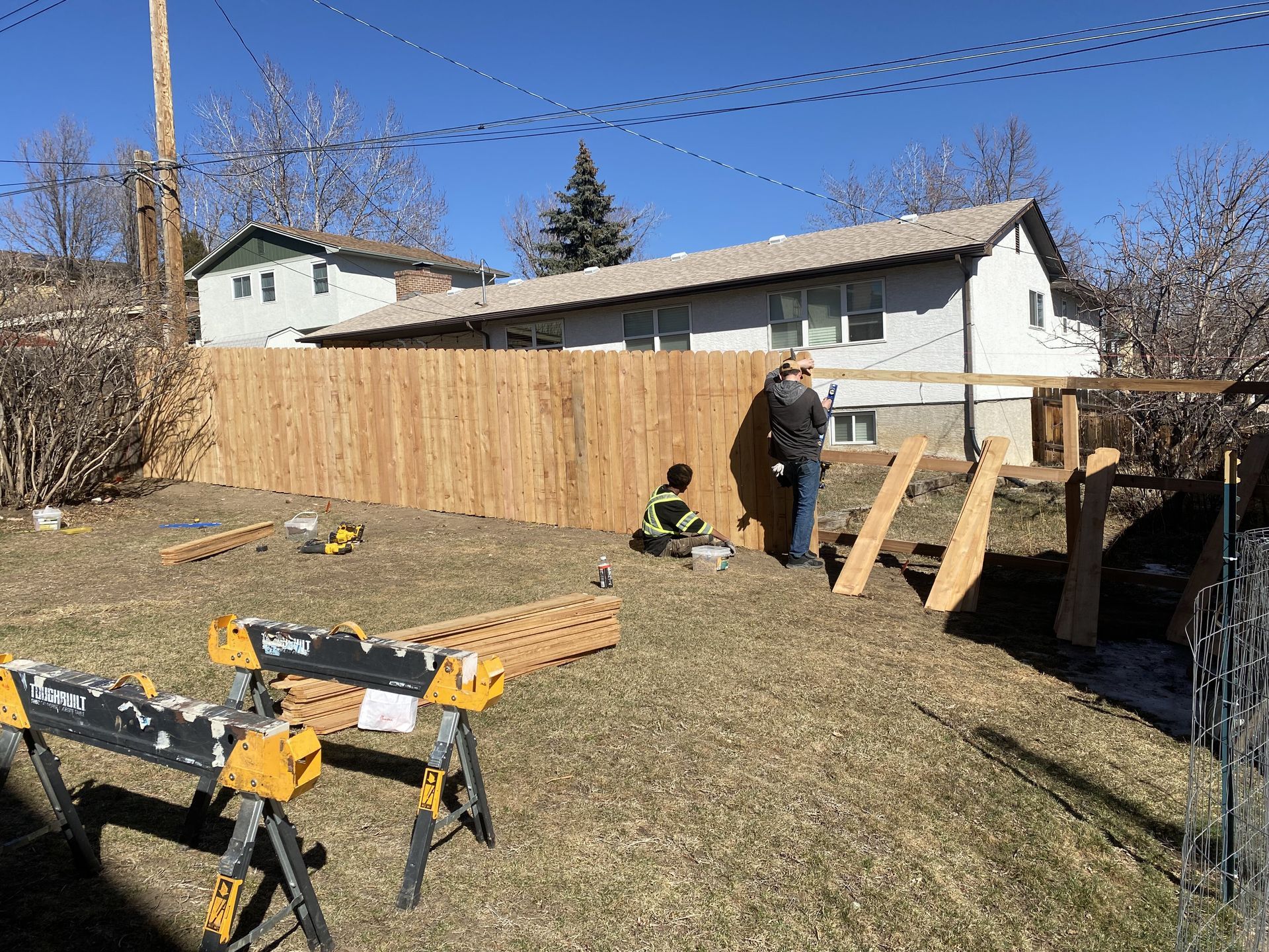 A man is building a wooden fence in the backyard of a house.
