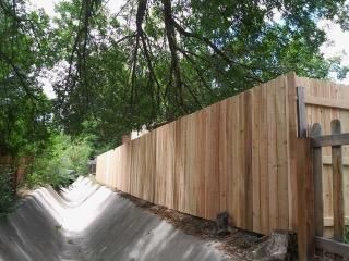 A wooden fence is surrounded by trees on the side of a road.