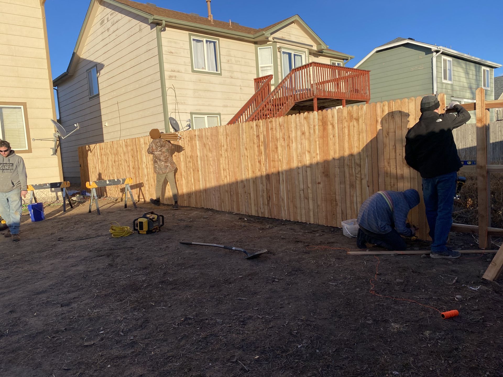 A group of people are working on a wooden fence in front of a house.