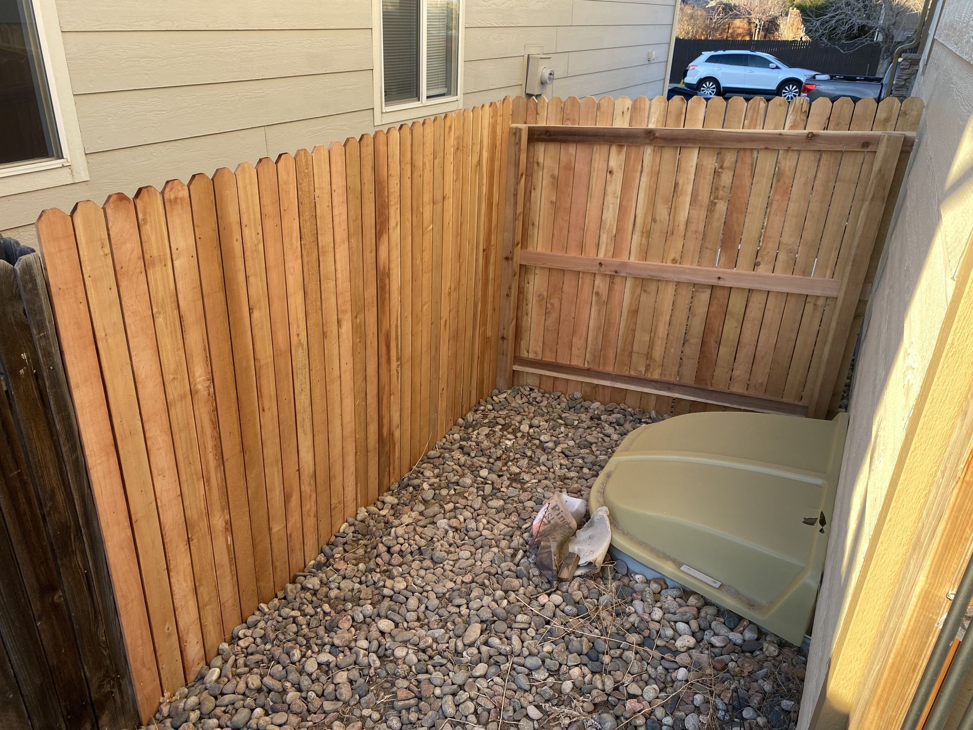 A wooden fence surrounds a gravel area in front of a house.