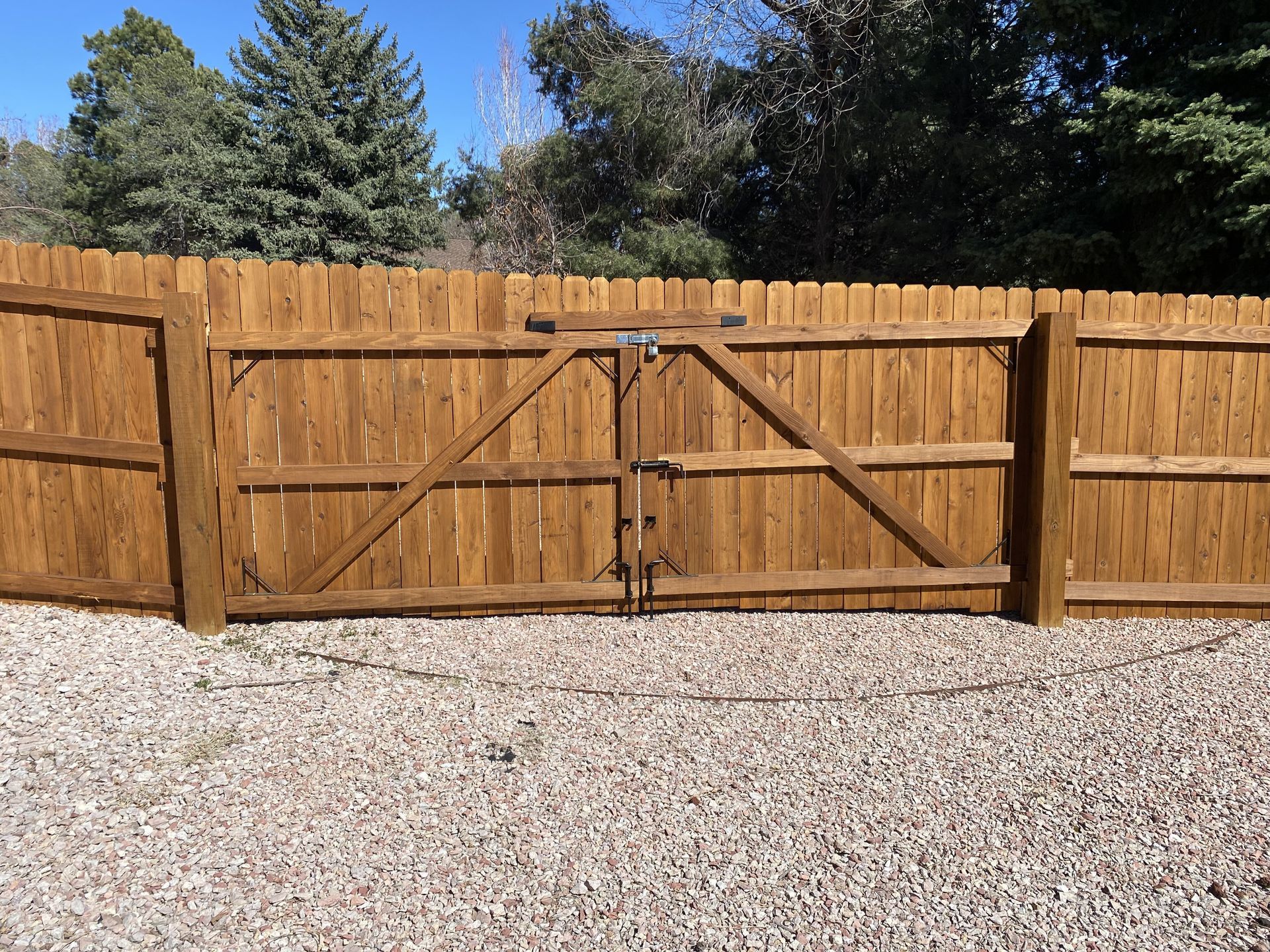 A wooden fence with a gate is surrounded by gravel.