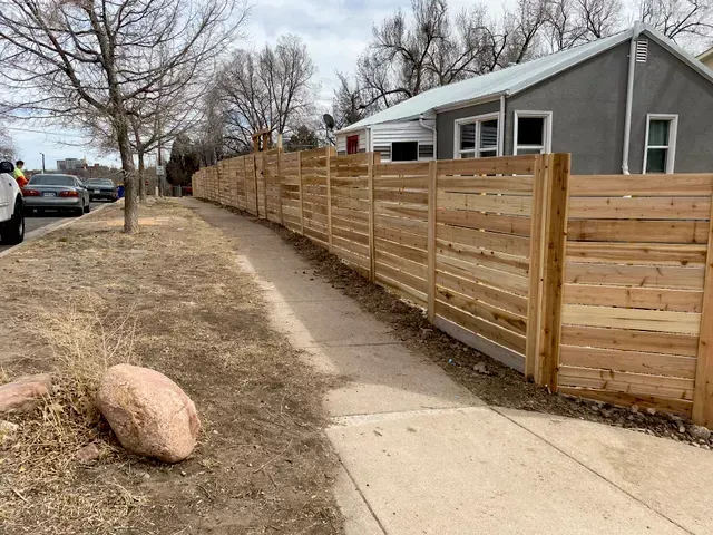 A wooden fence along a sidewalk next to a house.