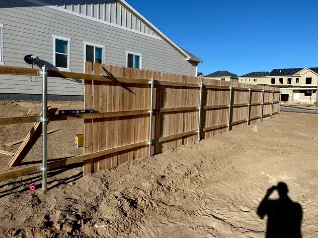 A wooden fence is being built in front of a house under construction.