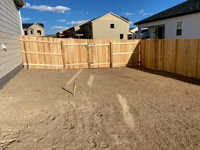 A wooden fence is in the backyard of a house.