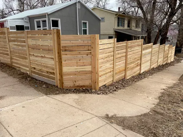 A wooden fence is surrounding a sidewalk in front of a house.