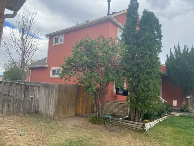 A red house with a wooden fence and trees in front of it.
