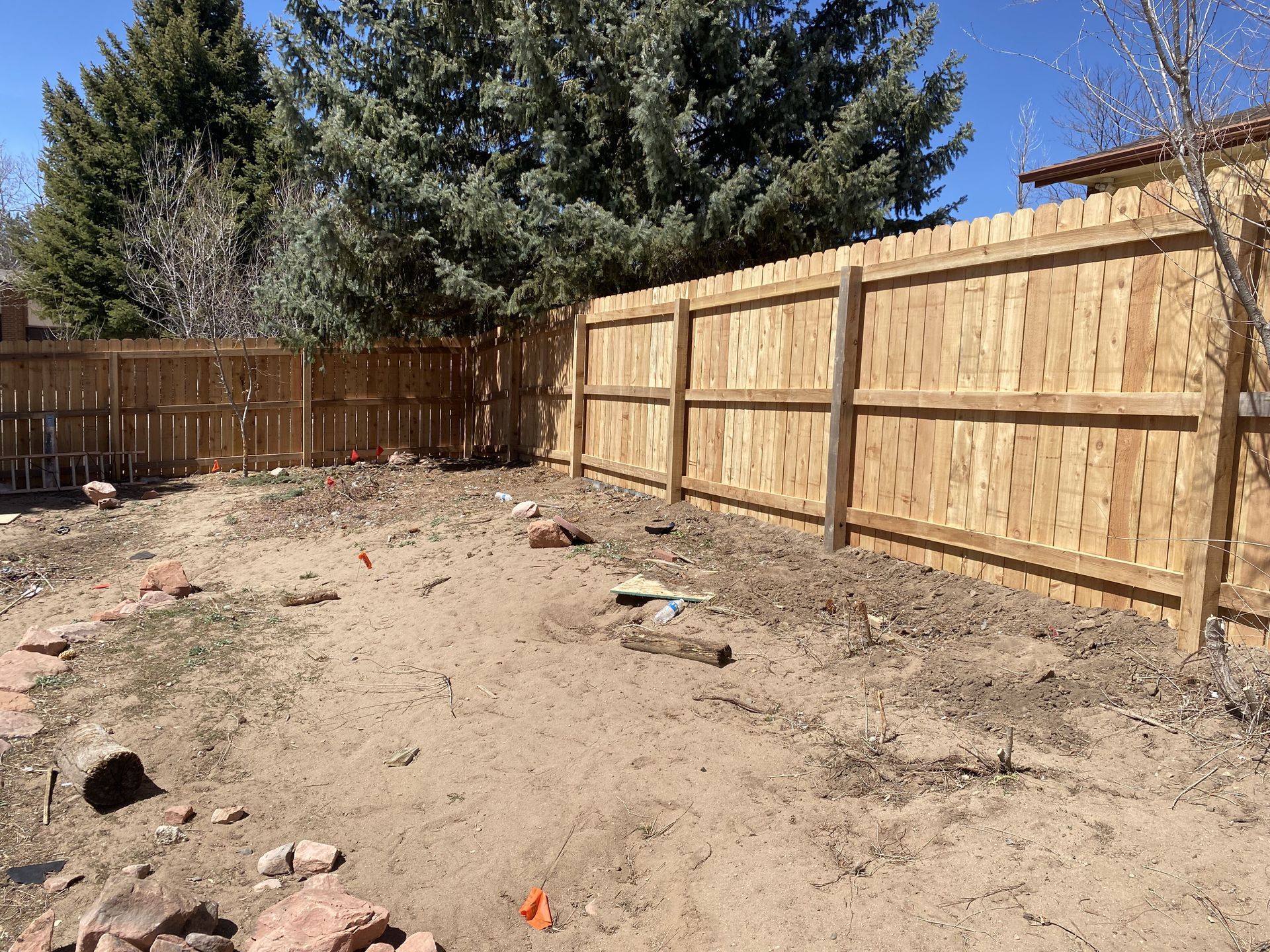 A wooden fence surrounds a dirt yard with trees in the background.