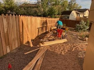 A man is working on a wooden fence in a backyard.