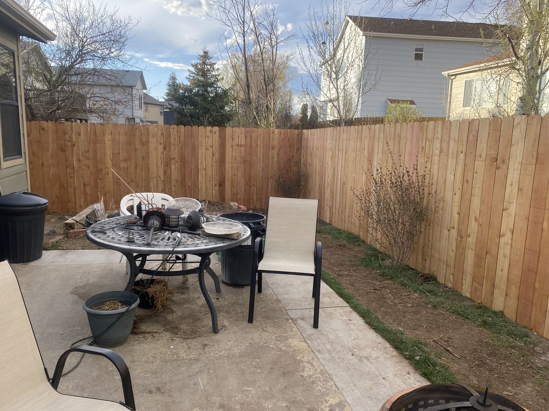 A wooden fence surrounds a patio with a table and chairs.