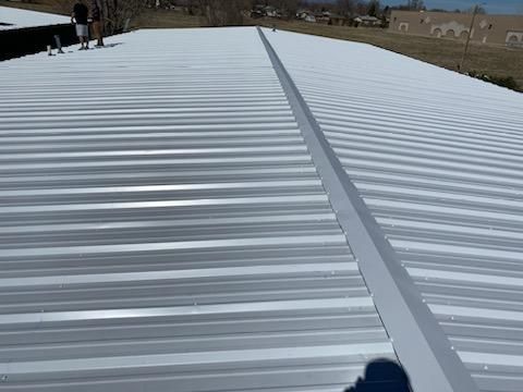 A person is standing on top of a white metal roof.