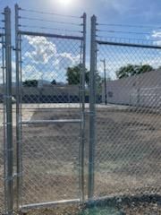 A chain link fence with a gate in the middle of a dirt field.