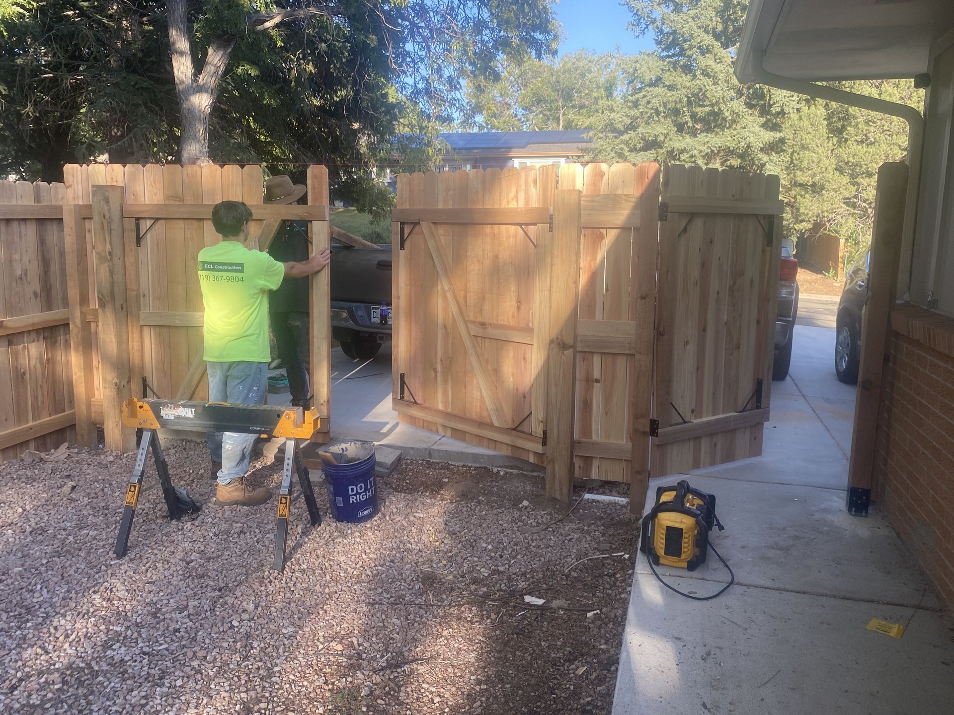 A man is working on a wooden fence in front of a house.