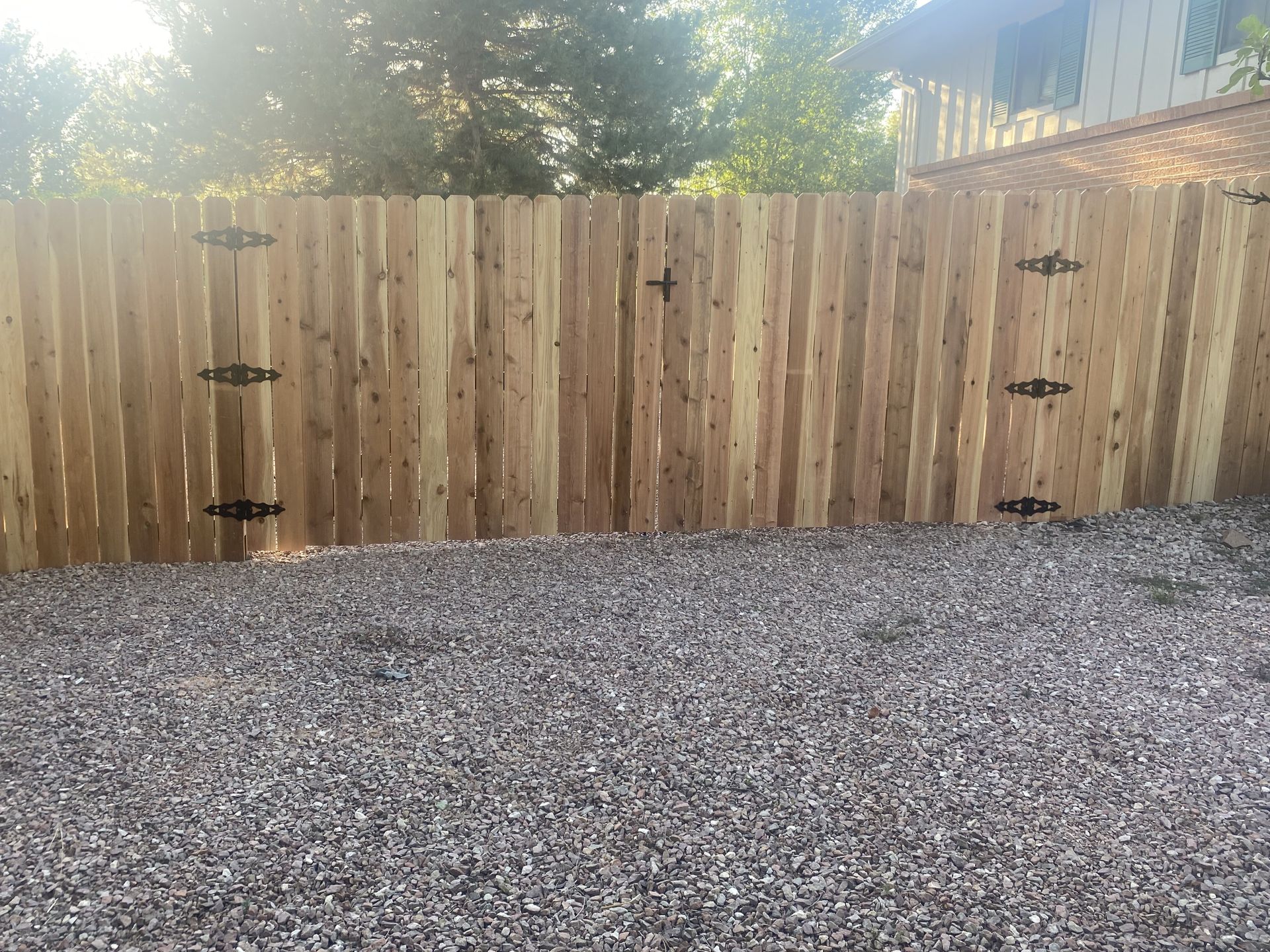 A wooden fence is surrounded by gravel and a house in the background.