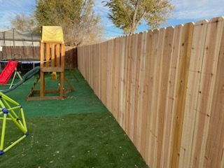 A wooden fence surrounds a playground with a slide and swings.
