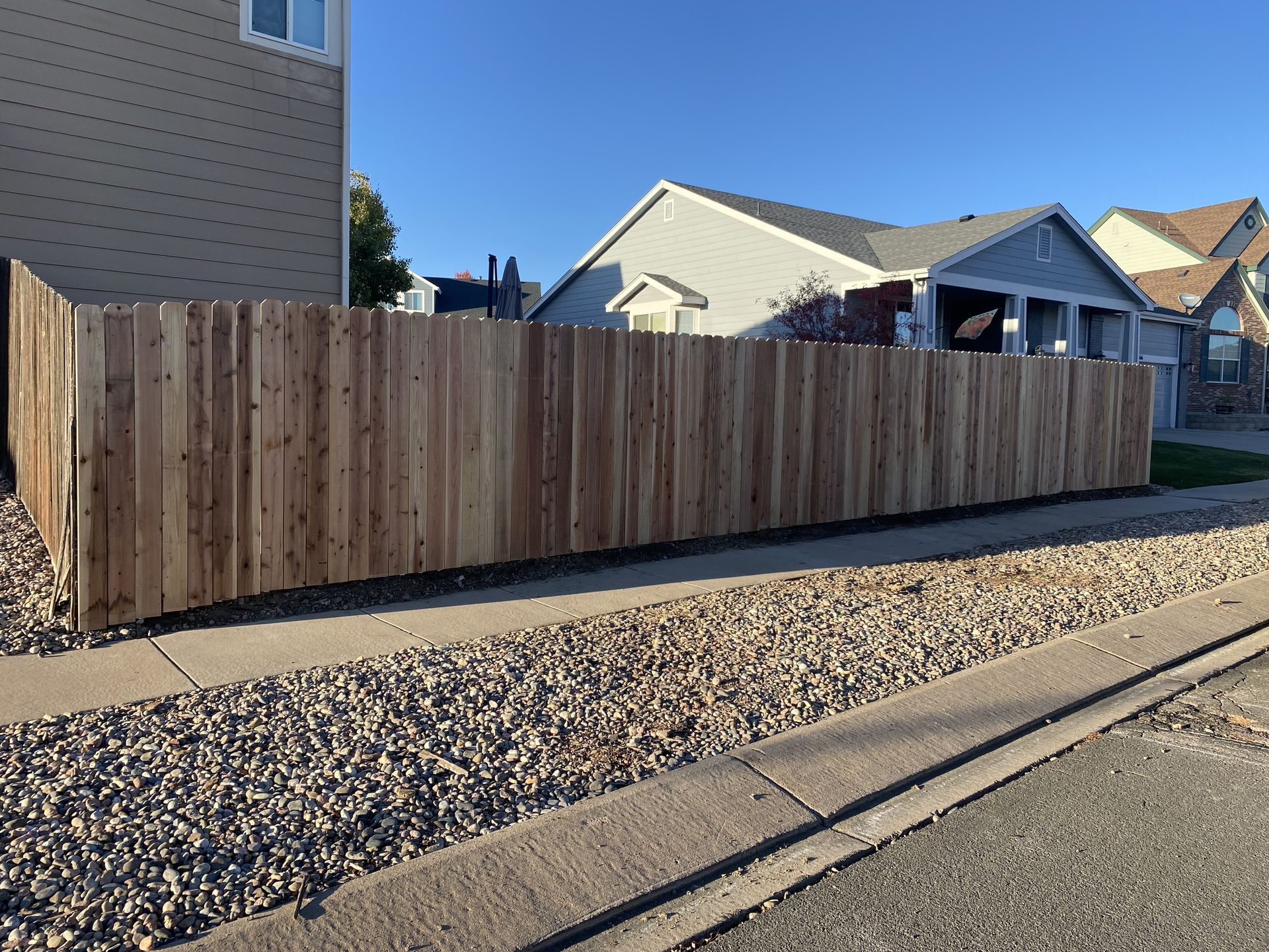 A wooden fence is sitting on the side of the road next to a house.
