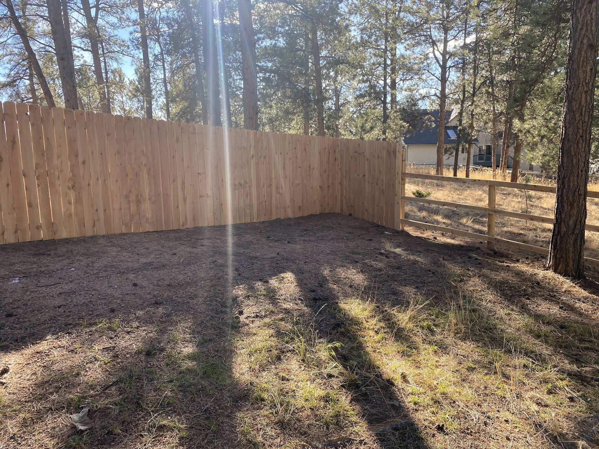 A wooden fence surrounds a dirt yard in the woods.