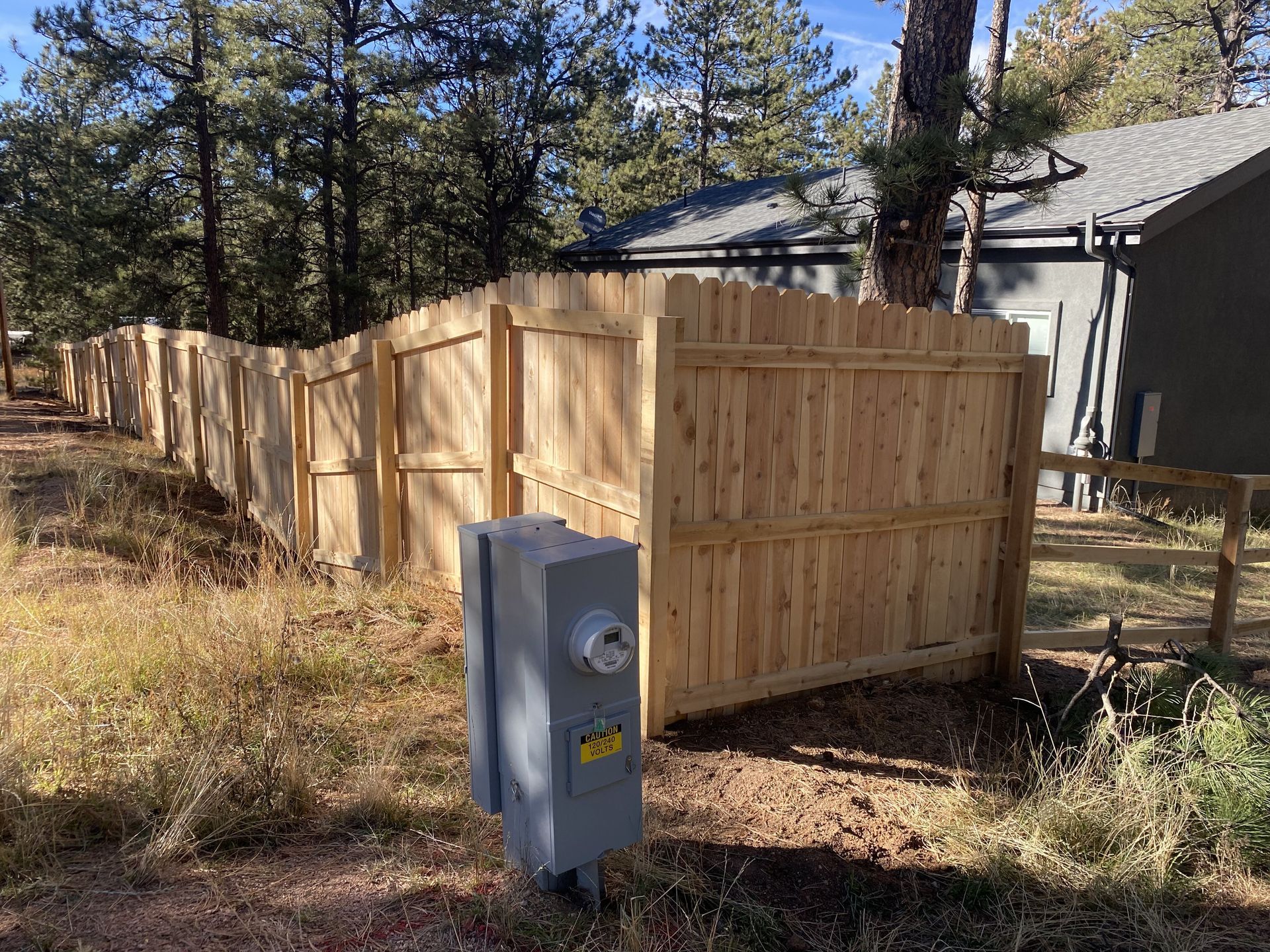 A wooden fence is surrounded by trees and a house.