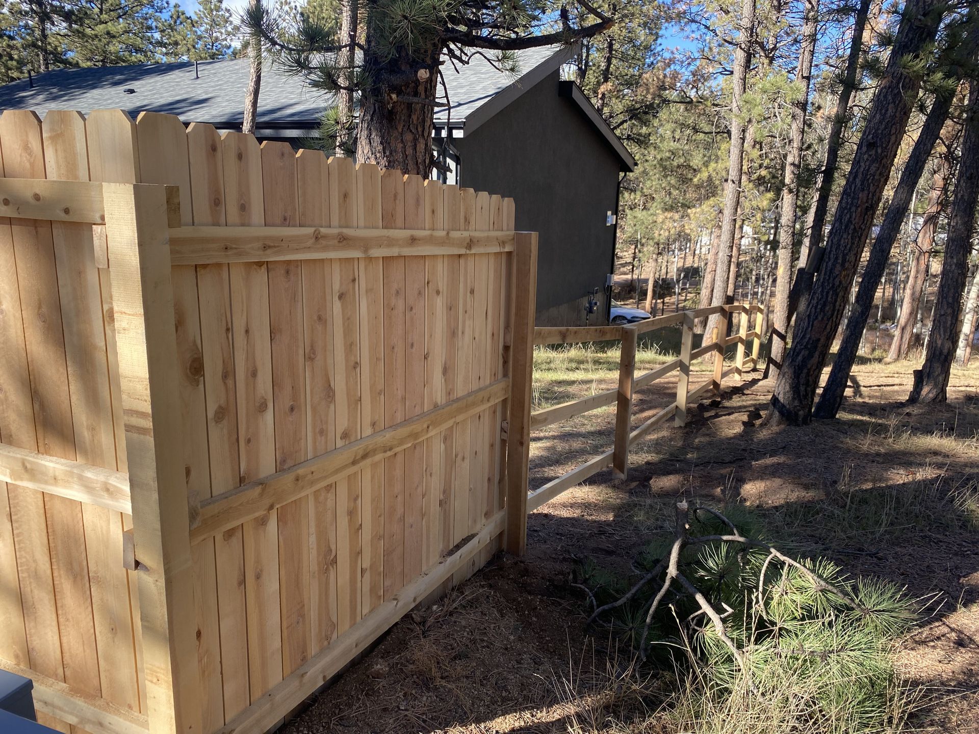 A wooden fence is surrounded by trees and a house in the background.