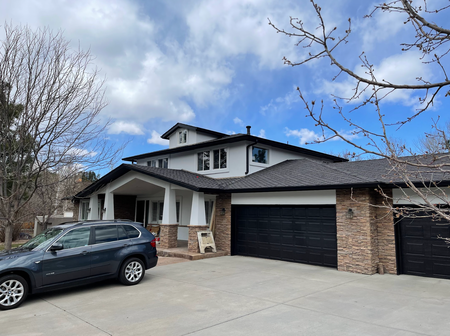 A car is parked in front of a large house with two garages.