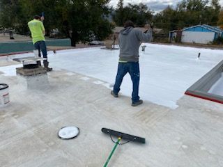 Two men are standing on a roof painting it white.