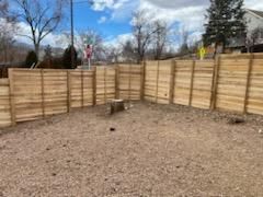 A wooden fence surrounds a gravel area in a backyard.