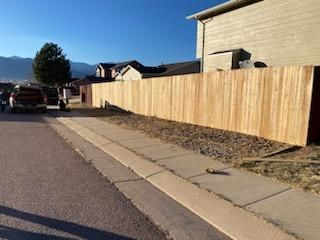 A wooden fence is sitting on the side of the road next to a sidewalk.