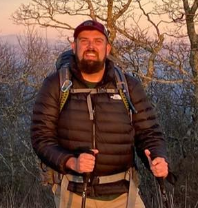 A man with a backpack and hiking poles is standing on top of a hill.