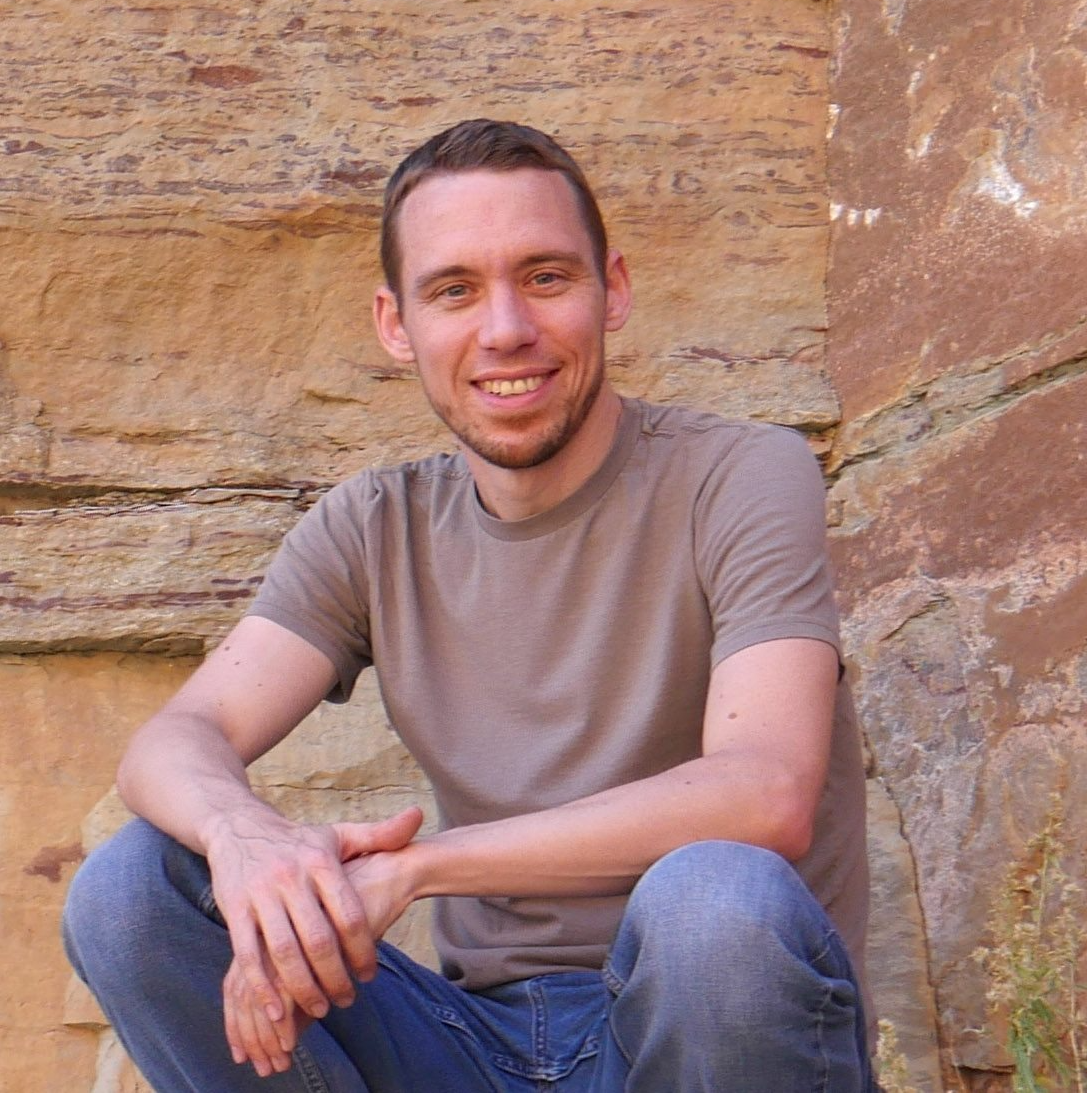 A man in a brown shirt sits on a rock wall