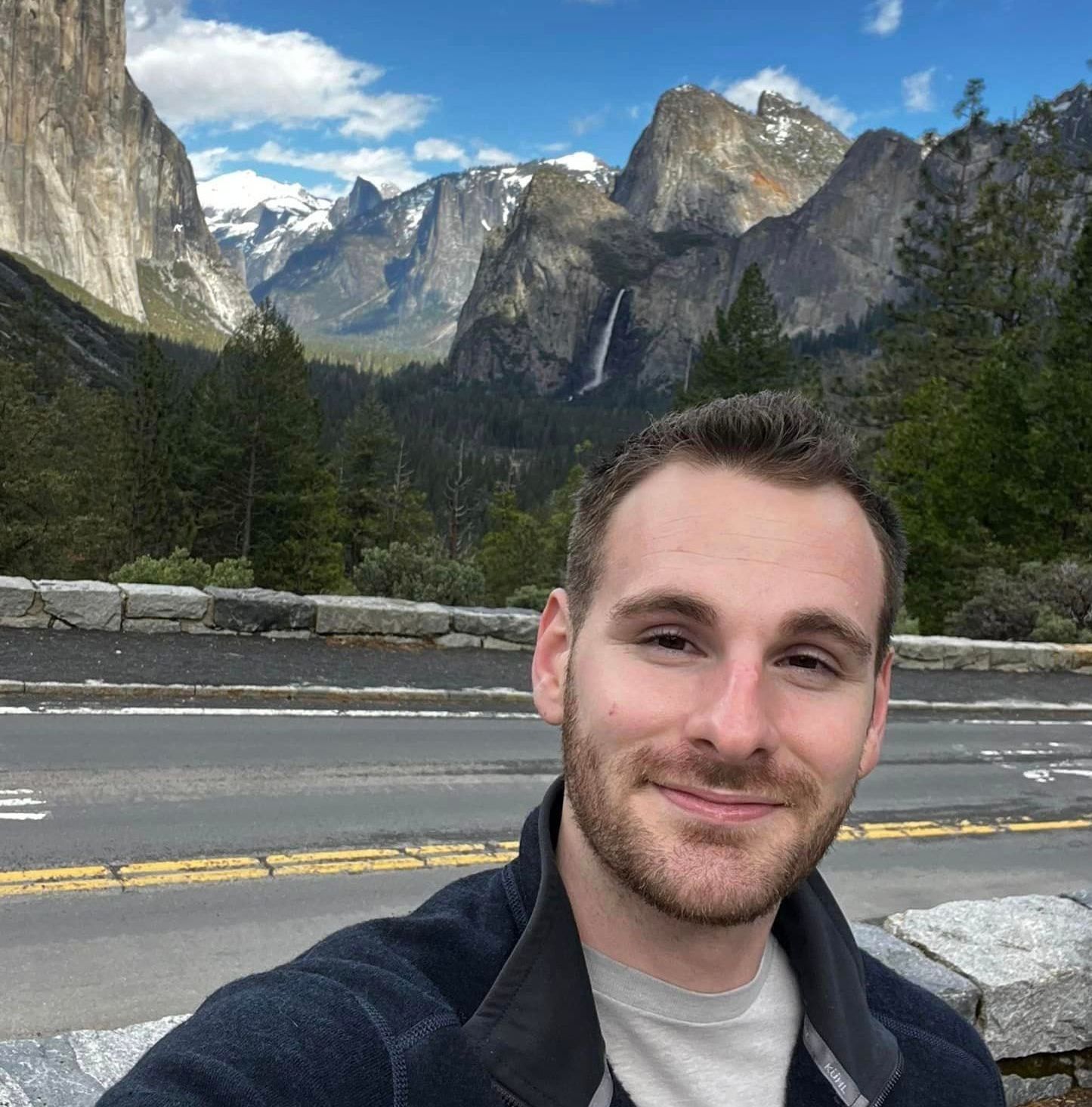 A man is taking a selfie in front of a mountain range.