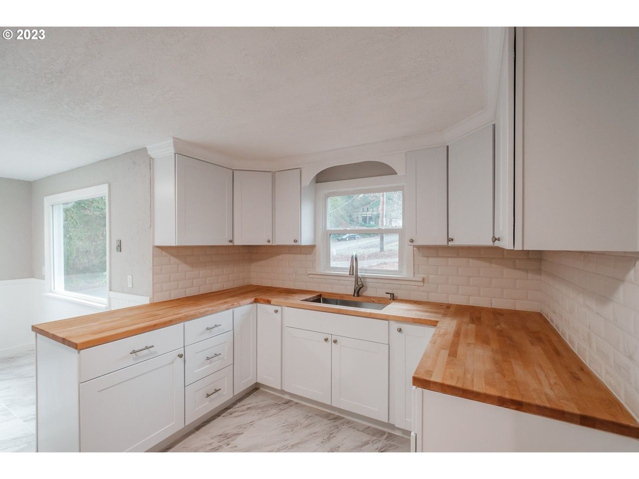 An empty kitchen with white cabinets and wooden counter tops.