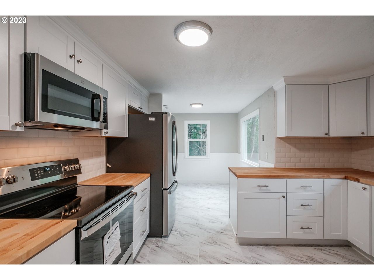 A kitchen with white cabinets , stainless steel appliances , and wooden counter tops.