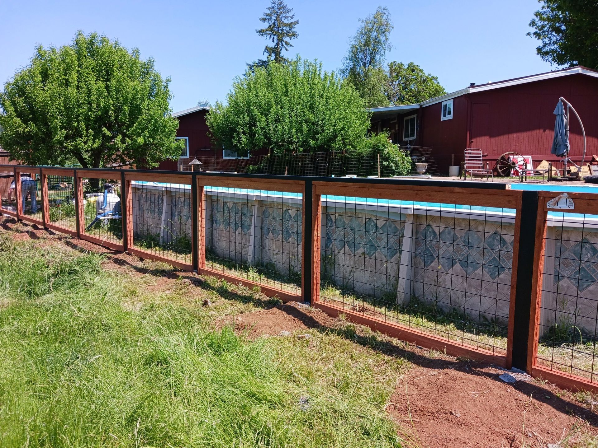 A wooden fence surrounds a swimming pool in a backyard.