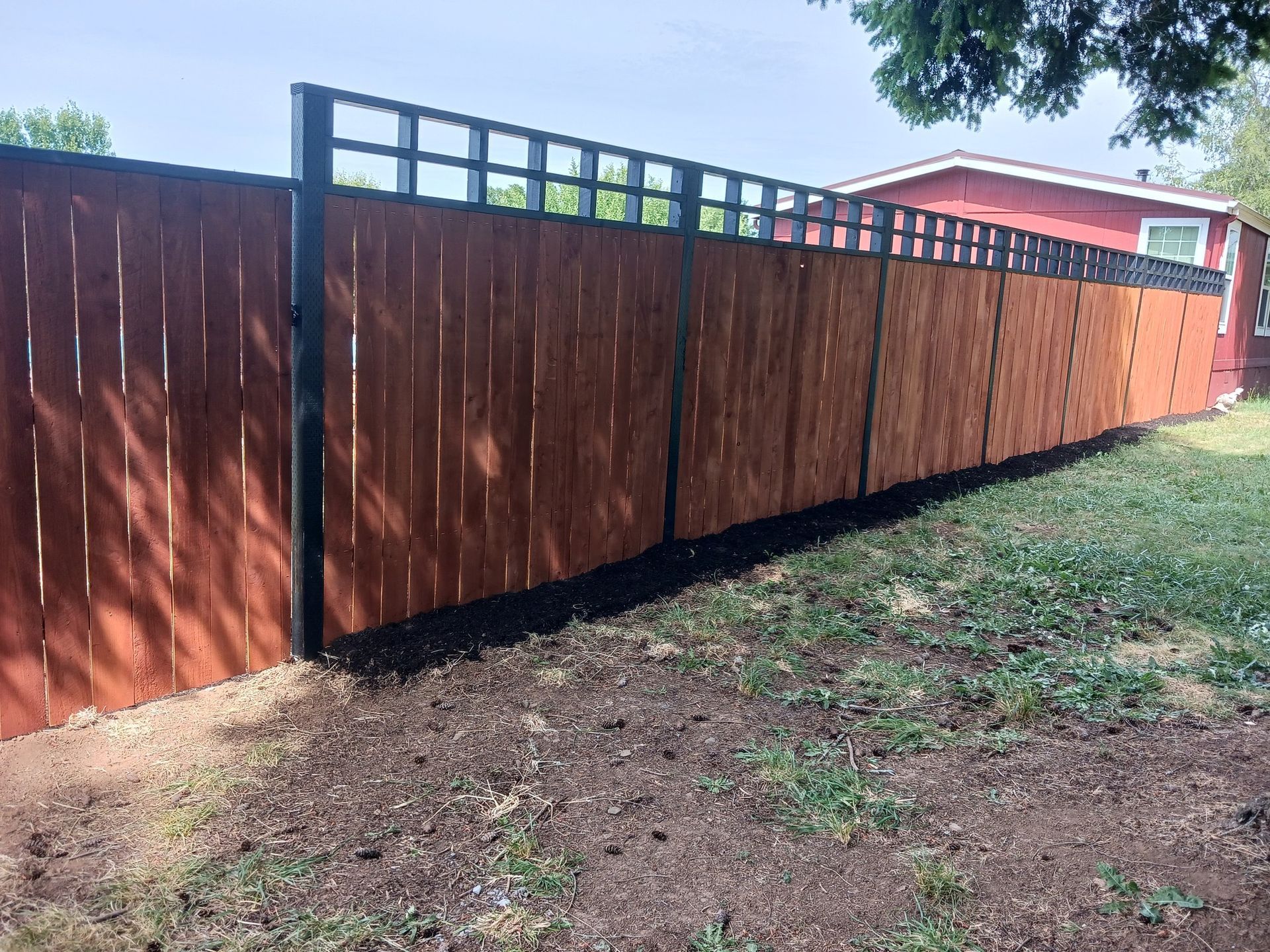 A wooden fence surrounds a lush green yard in front of a red house.
