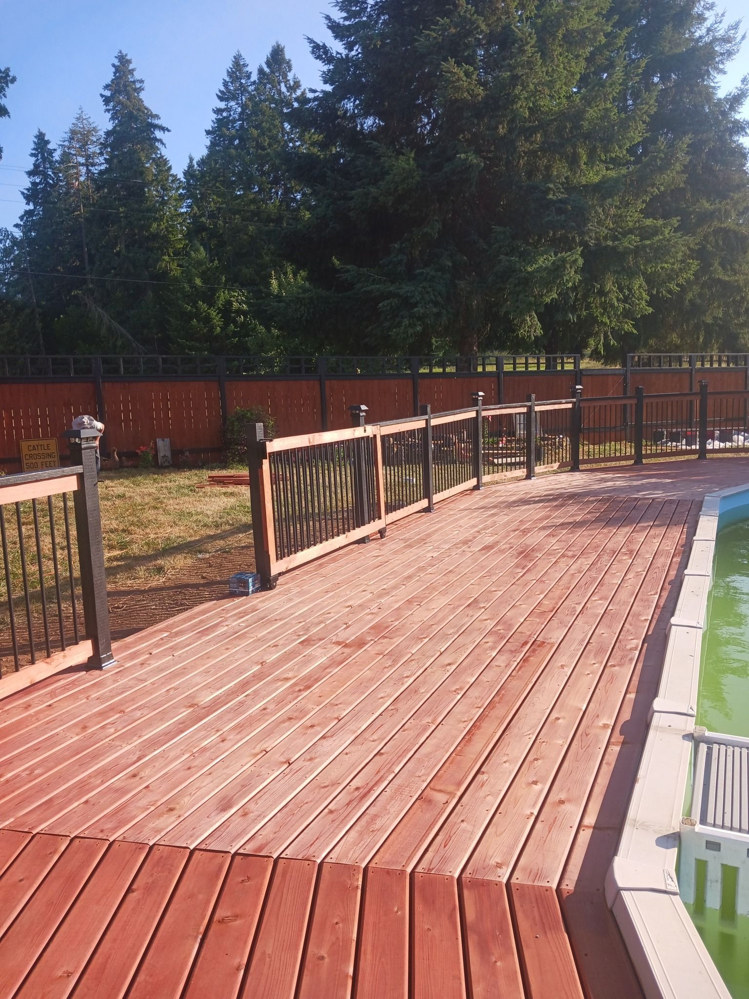 A wooden deck next to a pool with trees in the background