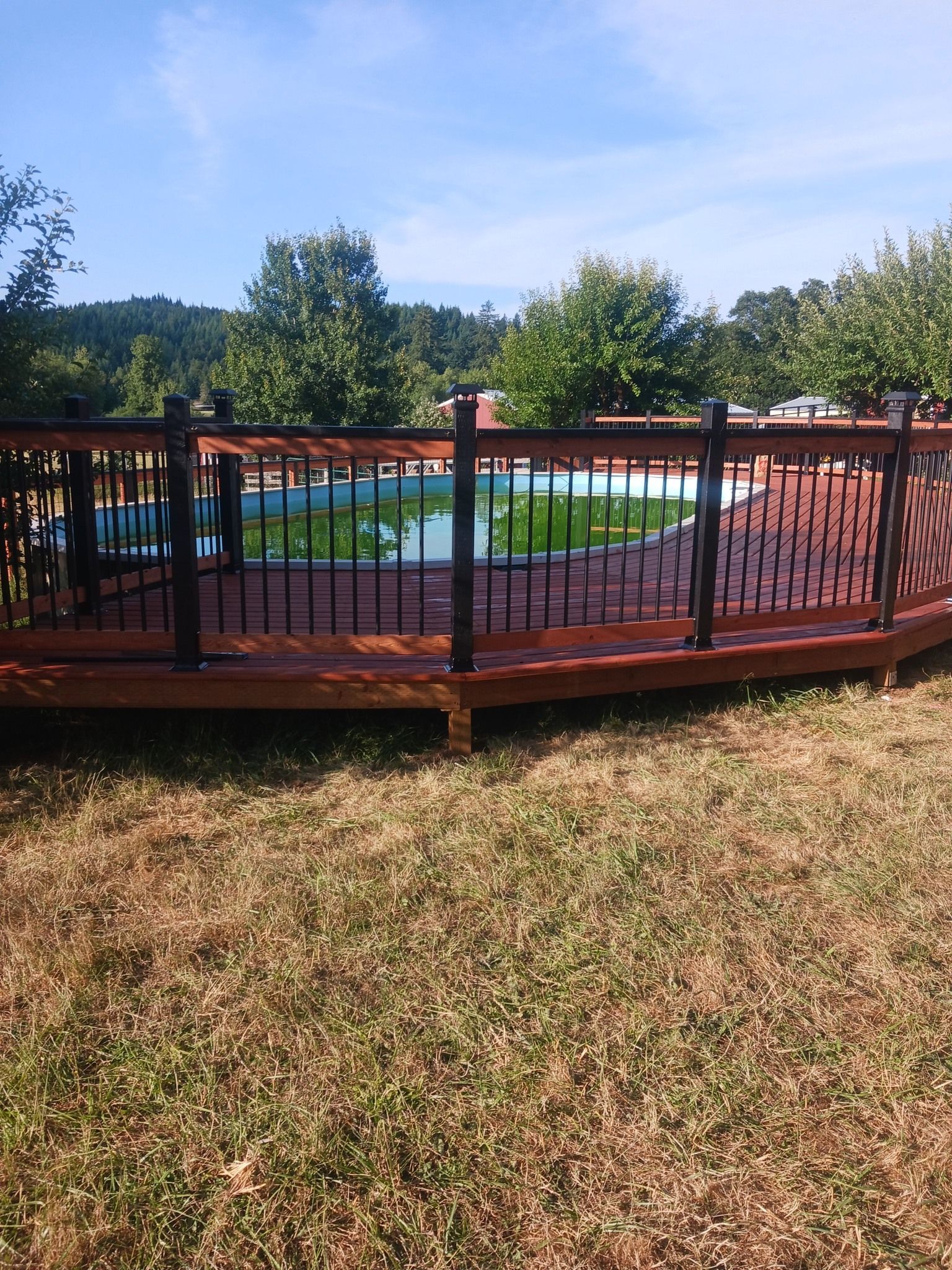 A wooden deck with a metal railing overlooking a swimming pool