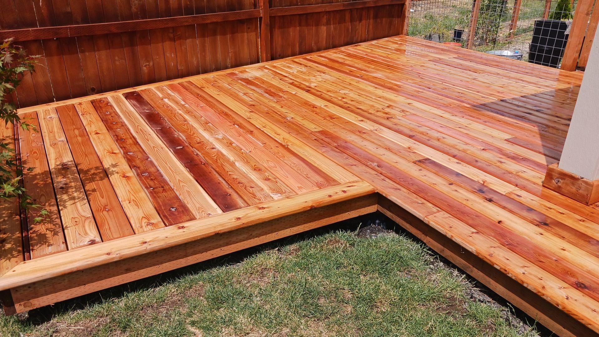 A wooden deck with a bench and a fence in the background.
