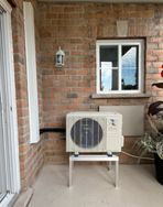 Un climatiseur blanc est posé sur un mur de briques à côté d'une fenêtre.
