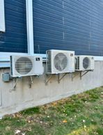 Trois climatiseurs sont montés sur le côté d'un bâtiment.