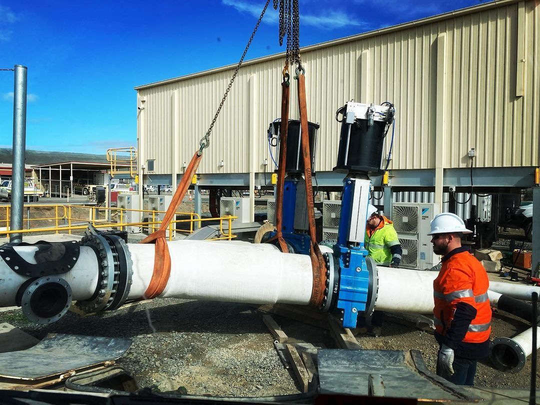 A Man In A Hard Hat Is Standing Next To A Large Pipe Being Lifted By A Crane — Blackpoly Pipelines in Dubbo, NSW