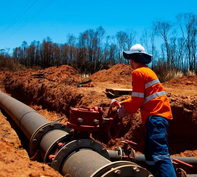 A Man In An Orange Shirt Is Working On A Pipe — Blackpoly Pipelines in Mount Isa, QLD