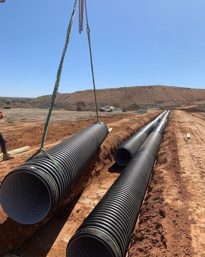 A Crane Is Lifting A Bunch Of Pipes In The Dirt — Blackpoly Pipelines in Orange, NSW