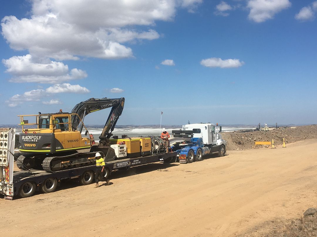 A Truck Is Carrying A Yellow Excavator On A Dirt Road — Blackpoly Pipelines in Orange, NSW