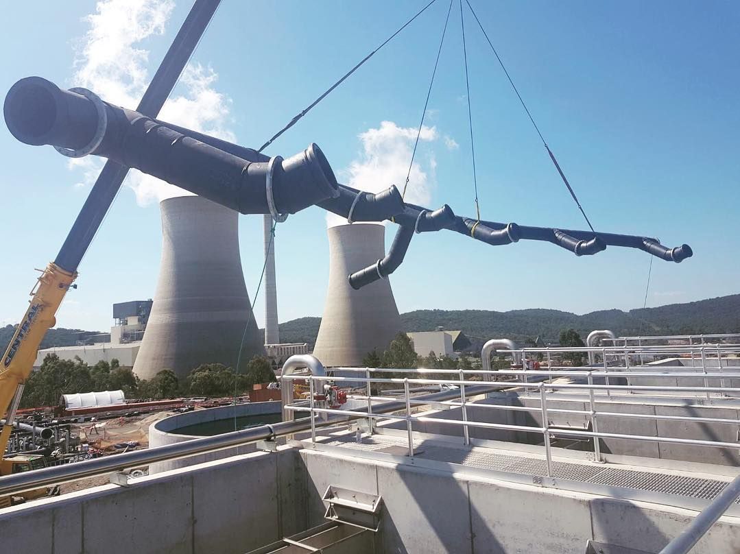 A Large Pipe Is Being Lifted By A Crane In Front Of Two Cooling Towers — Blackpoly Pipelines in Parkes, NSW