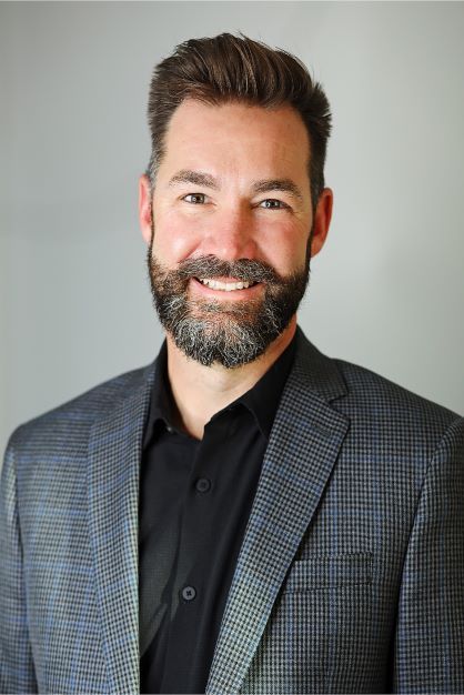 A man with a beard wearing a suit and black shirt